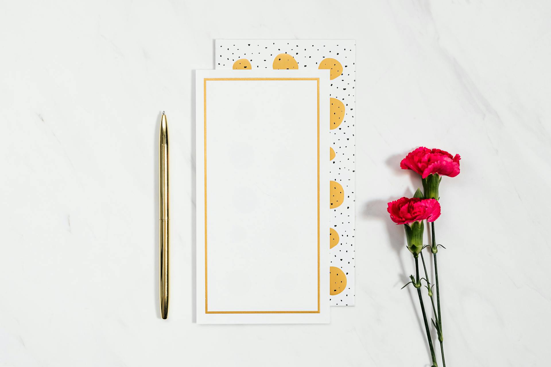 Sophisticated flat lay of a blank card, pen, and pink flowers on a white background, ideal for creative or business use.