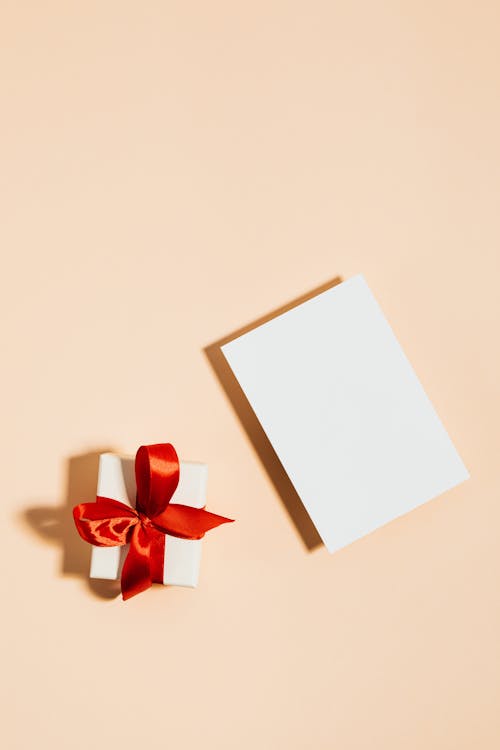 Gift Box With Red Ribbon and White Paper on Beige Background