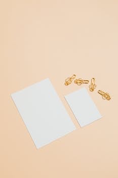 Minimalist setup showcasing white paper sheets and gold paperclips on a pastel background.