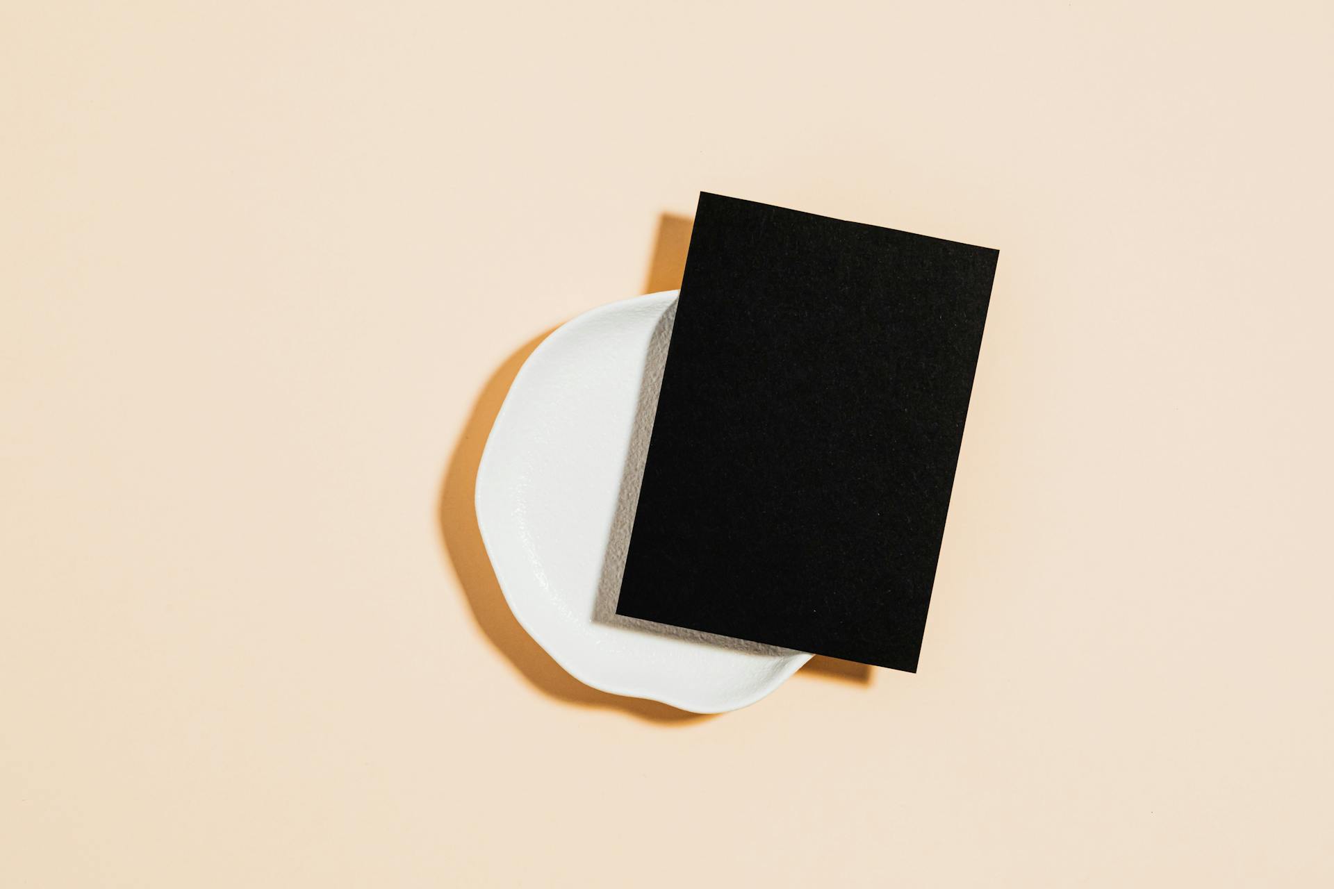 Minimalist mockup featuring a black card on a white plate against a neutral background, ideal for creative designs.