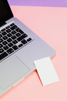 Minimalist photo of a silver laptop with blank paper against pink-purple tones, highlighting modern technology.