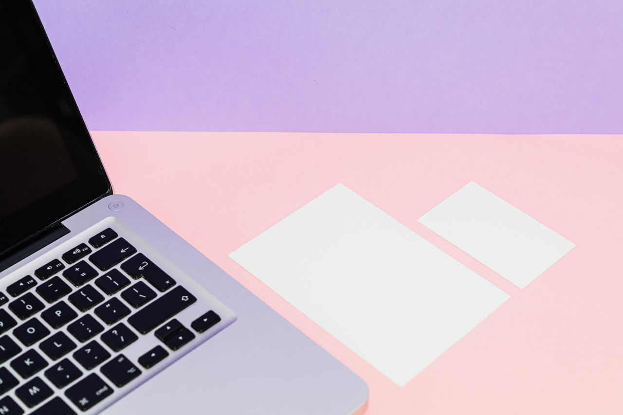 Flat lay of a laptop with blank cards on a pastel pink and purple background