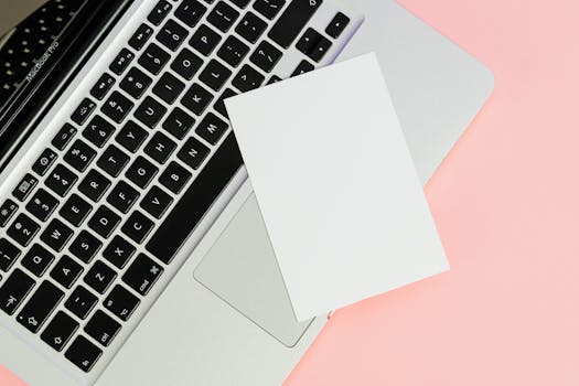 A blank card placed on a laptop keyboard with ample copy space on a pastel background.