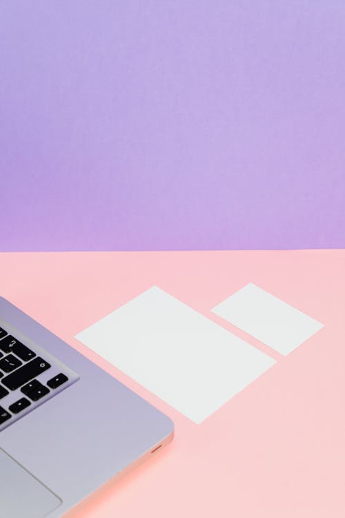 White Paper Beside a Laptop on Pink an Purple Background