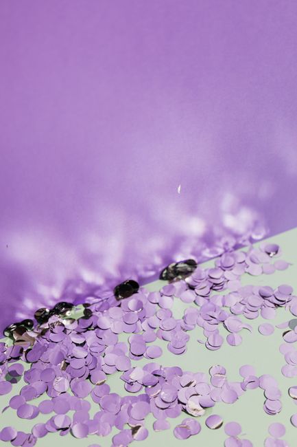 Sparkling purple confetti scattered on a lilac backdrop, creating a festive and playful scene.