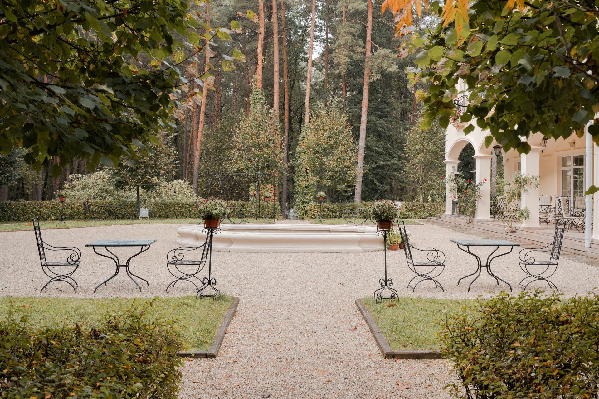 Serene garden courtyard with iron furniture surrounded by lush green trees and mansion architecture.