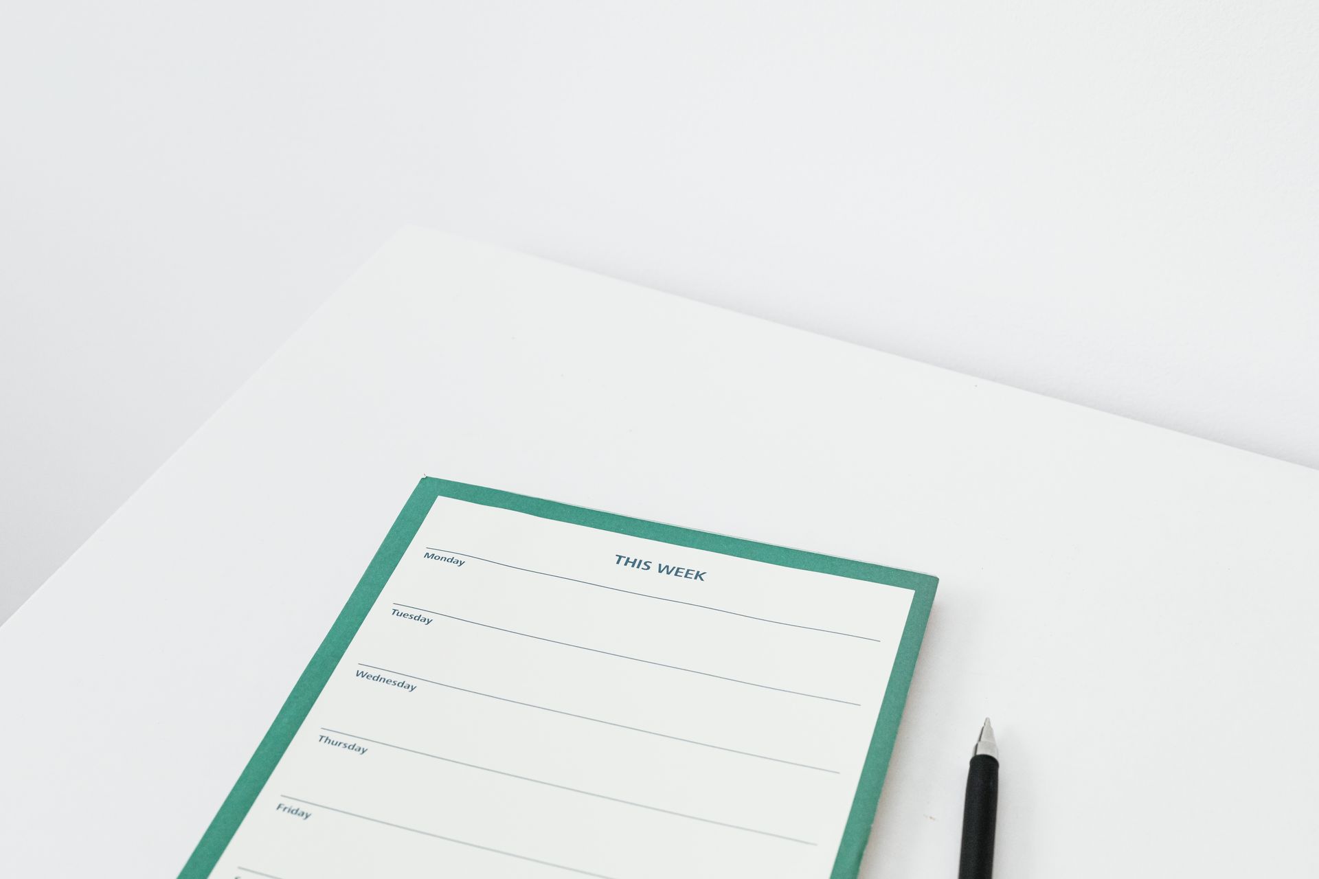 A clean and minimalist weekly planner with a pen on a white desk, perfect for organizing your schedule efficiently.
