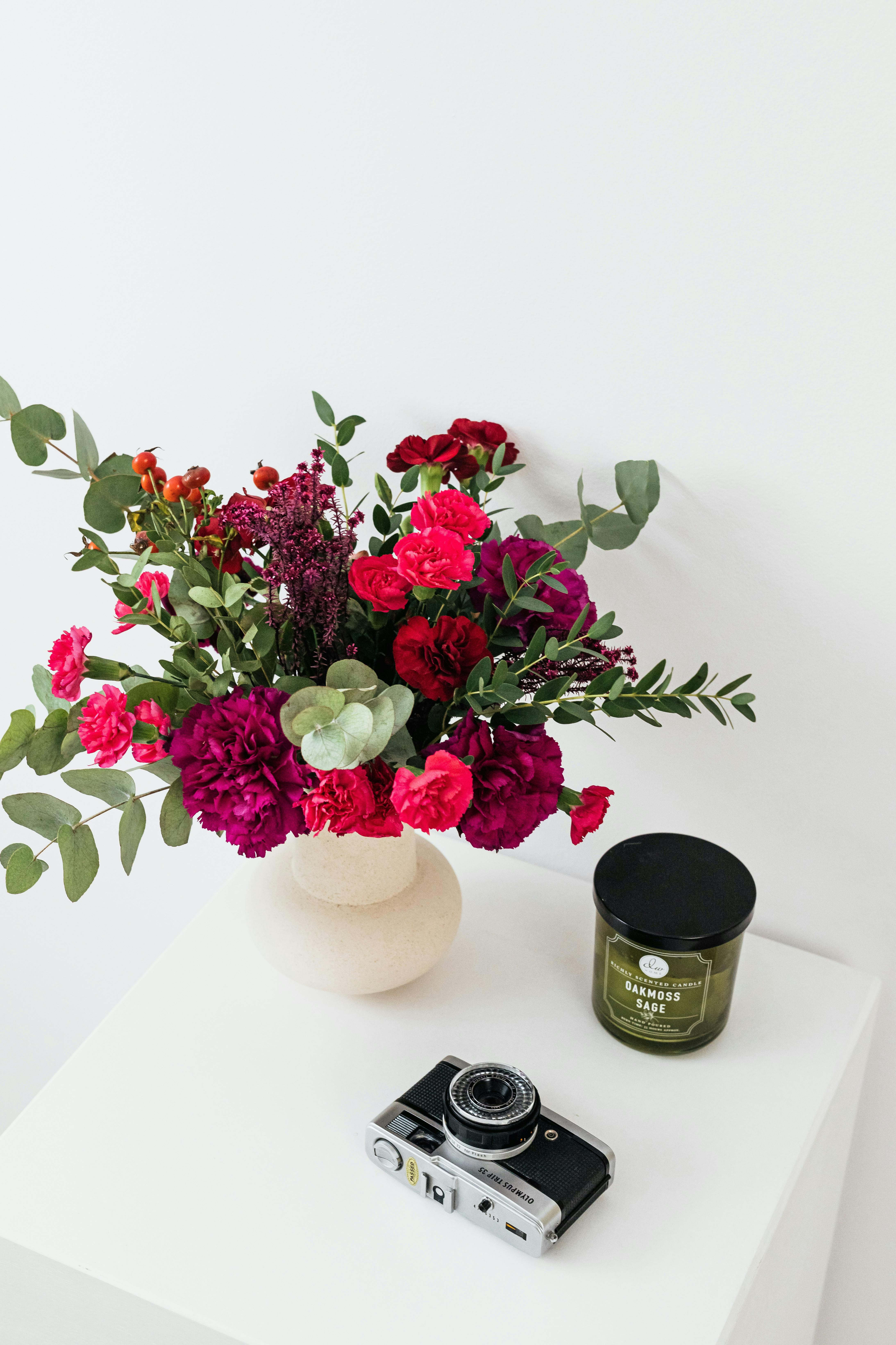 Charming floral arrangement in a vase beside a vintage camera and scented candle.