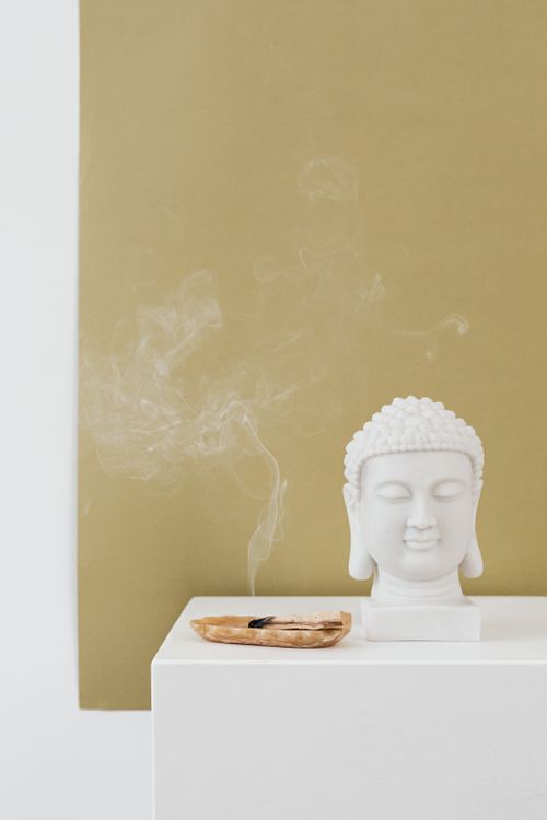 Free A white Buddha sculpture with incense smoke against a soft beige background, offering tranquility. Stock Photo