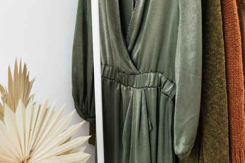 Free Stylish green dress on a clothes rack with knitted sweaters and dried leaves in a cozy setting. Stock Photo