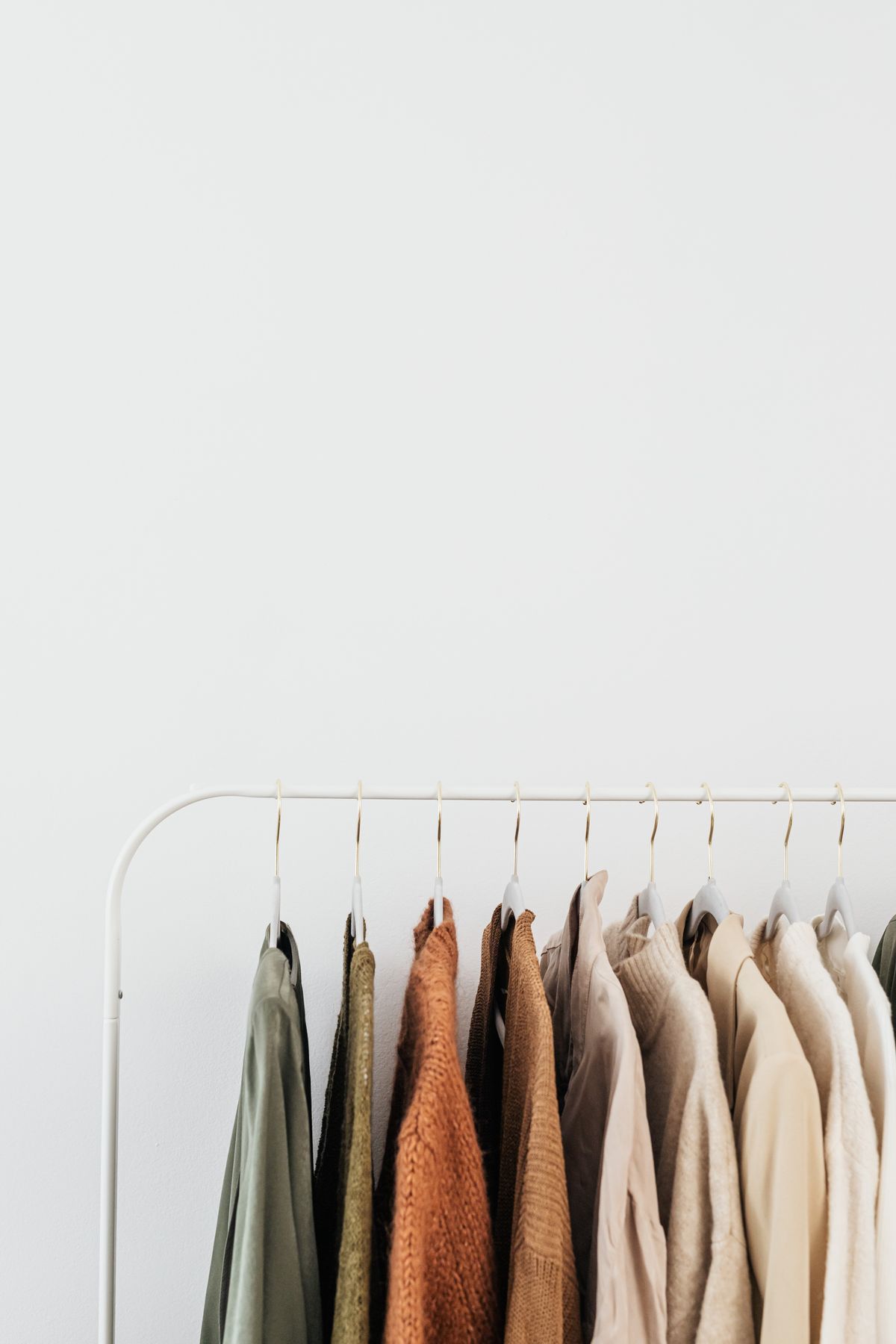 Neutral-toned shirts and jackets hanging on a white clothing rail
