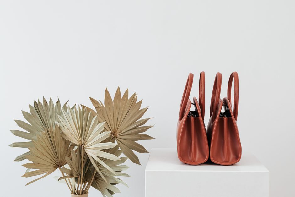 Elegant brown handbags alongside dried palm leaves on white background.