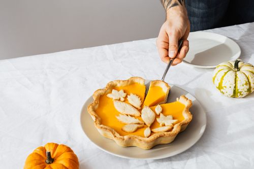 Free A hand cutting a festive pumpkin pie with decorative crust on a table with small pumpkins. Stock Photo