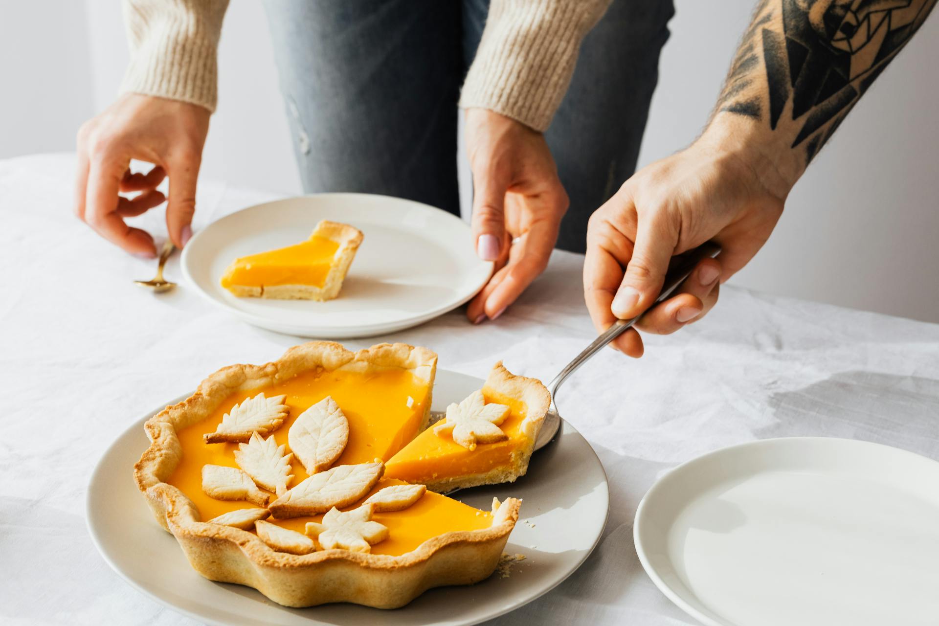 Close-up of two people serving pumpkin pie slices on plates, showcasing desserts with leaf designs.