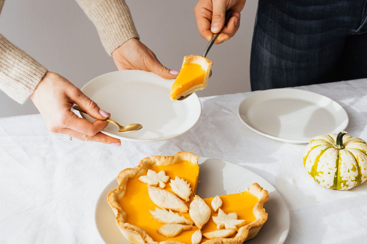 Hands serving a slice of decorated pumpkin pie at a set table