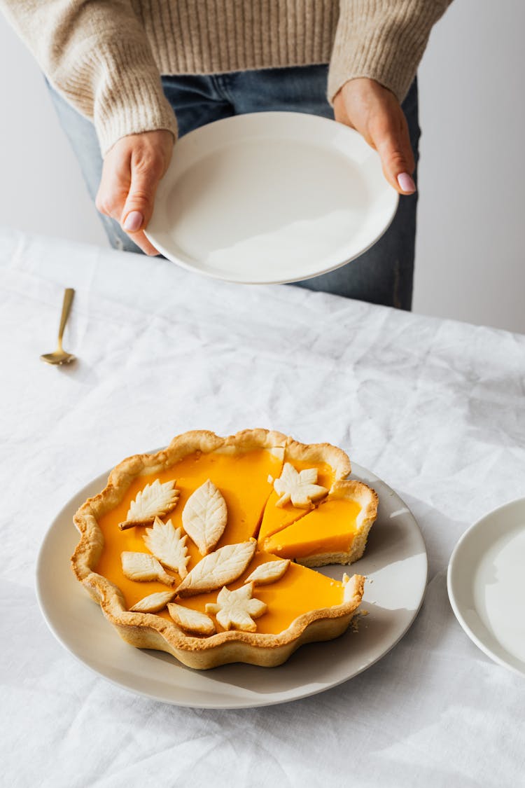 A Person Holding A Ceramic Plate Near The Table With Sliced Pie