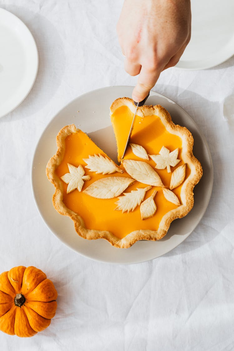 A Person Slicing A Pumpkin Pie On A Ceramic Plate