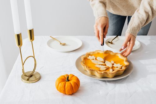 Free A festive autumn table setting with a homemade pumpkin pie being sliced, perfect for seasonal celebrations. Stock Photo