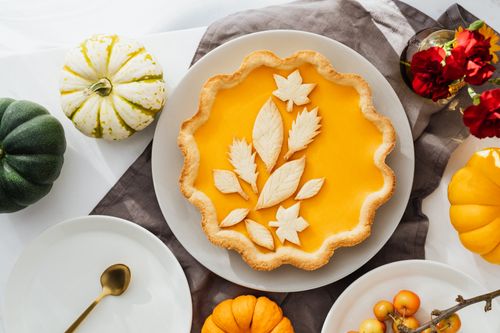Free Flat lay of a pumpkin pie with leaf-shaped pastry decorations, surrounded by small pumpkins and flowers. Stock Photo
