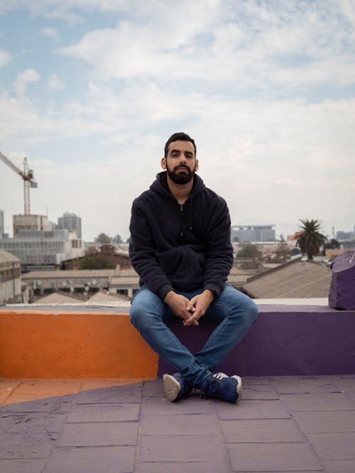 Man in Black Hoodie and Blue Denim Jeans Sitting on Rooftop