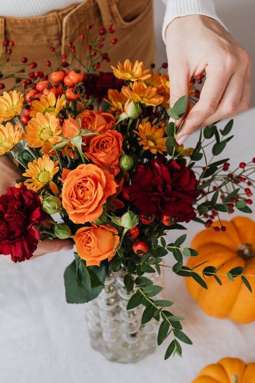 Free Vibrant autumn bouquet with oranges and reds in a glass vase, enhanced by seasonal decor. Stock Photo