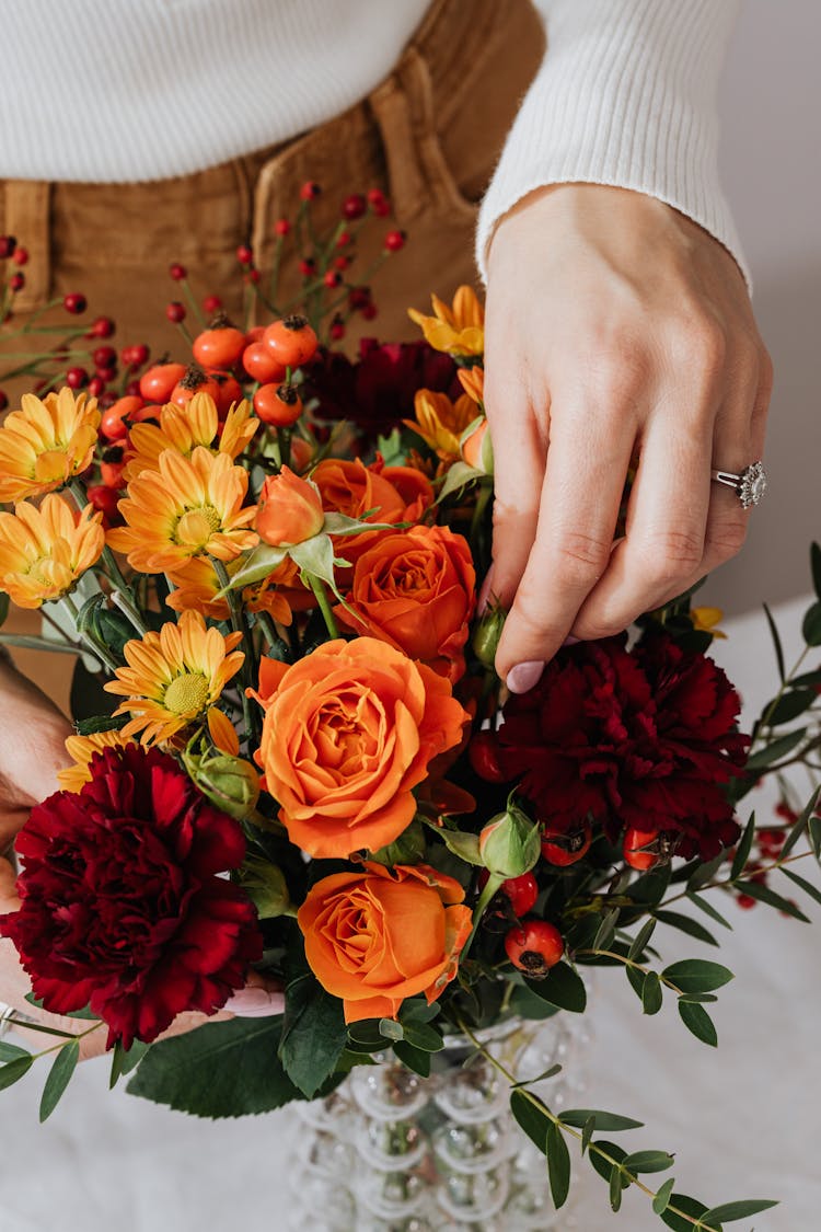 Person Arranging Flowers In A Glass Vase