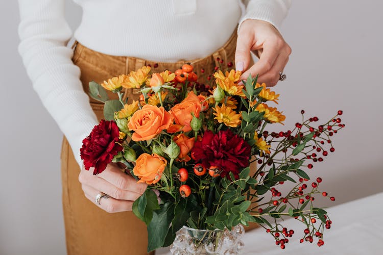 Woman In White Long Sleeve Shirt Arranging Red And Yellow Flowers In Vase