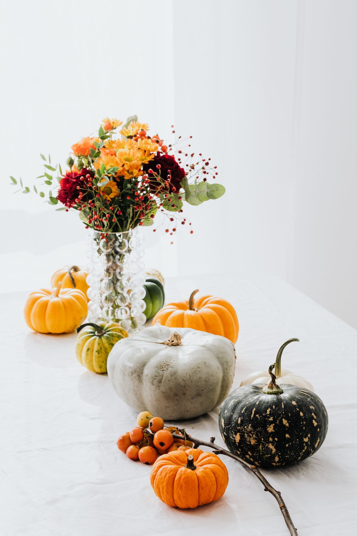 A serene autumn still life with pumpkins and vibrant floral arrangement in a glass vase. Stock Photo.