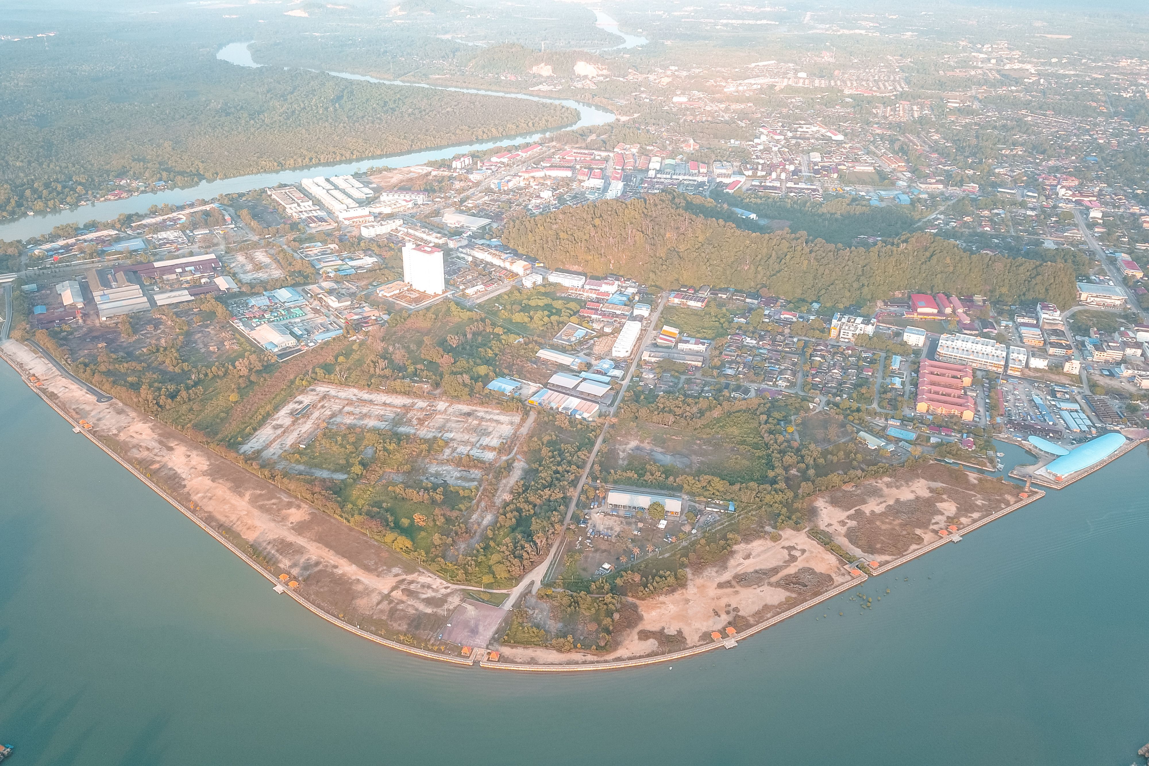 From above of long sandy snaking coastline of blue bay near town immersed in lush dark green forest