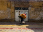 An Elderly Man Walking on the Street while Carrying a Heavy Sack and a Plastic Bag