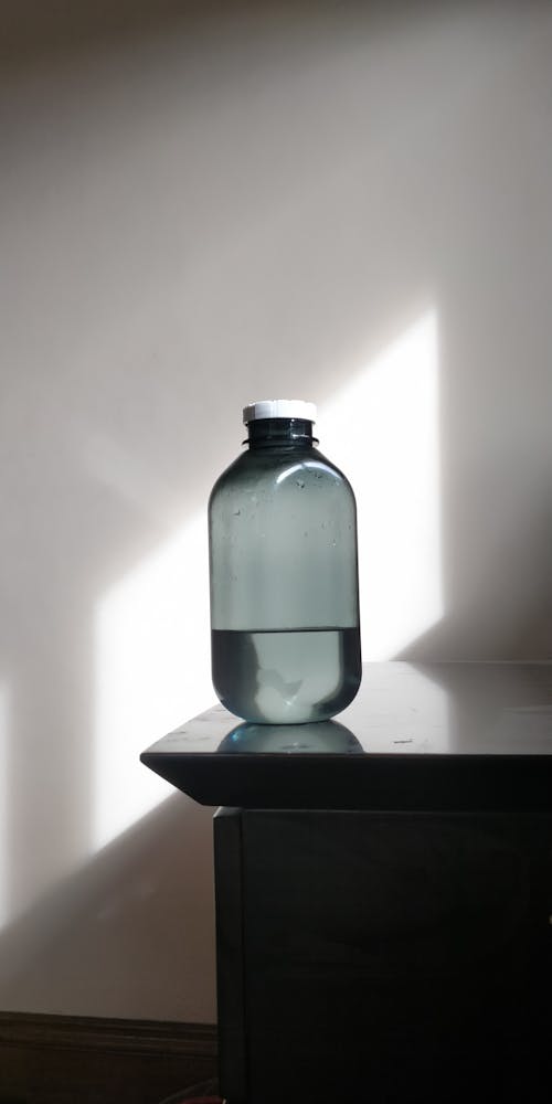 Free Gray Bottle with Water on Edge of a Wooden Table Stock Photo