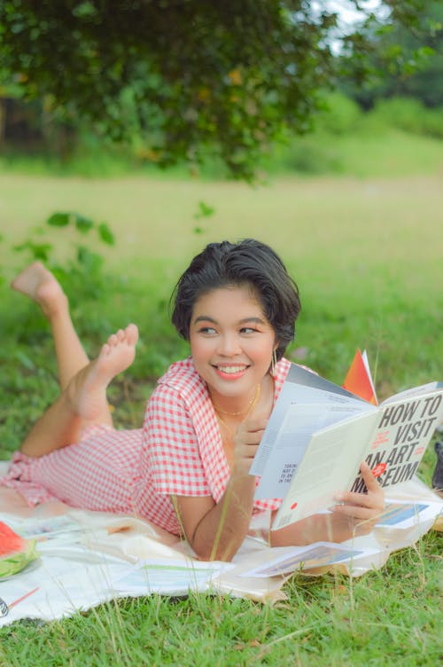 Woman Holding a Book While Lying on Blanket