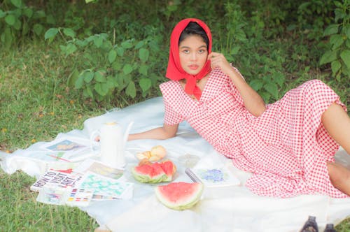 A Woman in Checkered Dress and Headscarf Lying on a Picnic Blanket