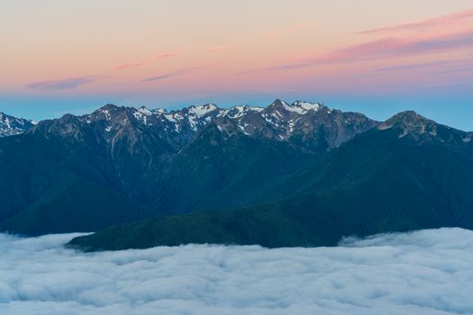 日出时分，从云层之上鸟瞰，白雪皑皑的山峰与戏剧性的天空共同勾勒出一片宁静的自然景象