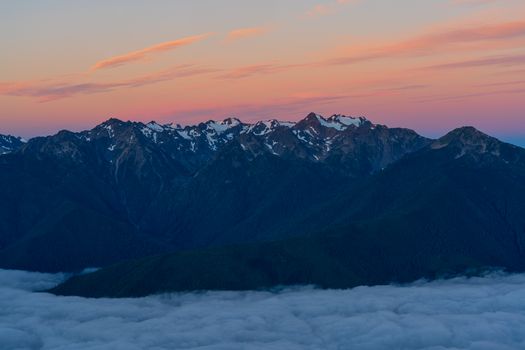 Snow-capped rock mountains at twilight with vibrant sky and misty valley below.