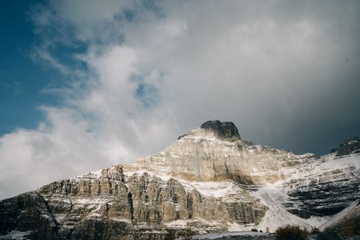 A stunning view of a snow-covered mountain peak under a vivid blue sky and dramatic clouds.