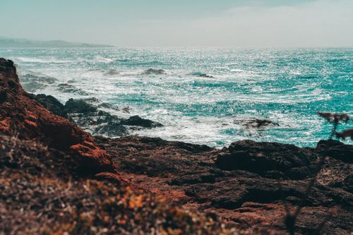 Free Breathtaking view of a rocky coastline with turquoise ocean and crashing waves under a bright sky. Stock Photo