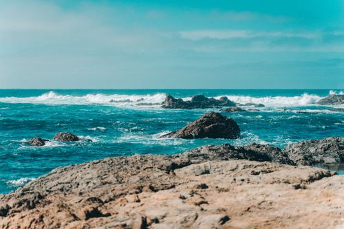 Free A breathtaking view of ocean waves crashing on rocky formations under a clear blue sky. Stock Photo