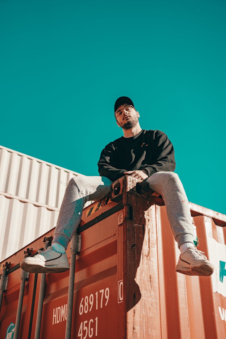 Bearded Man Sitting On Orange Cargo Container On Sunny Day