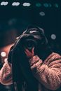 Unrecognizable person wearing hooded clothes and hiding face behind black scarf taking photo on professional camera on blurred background