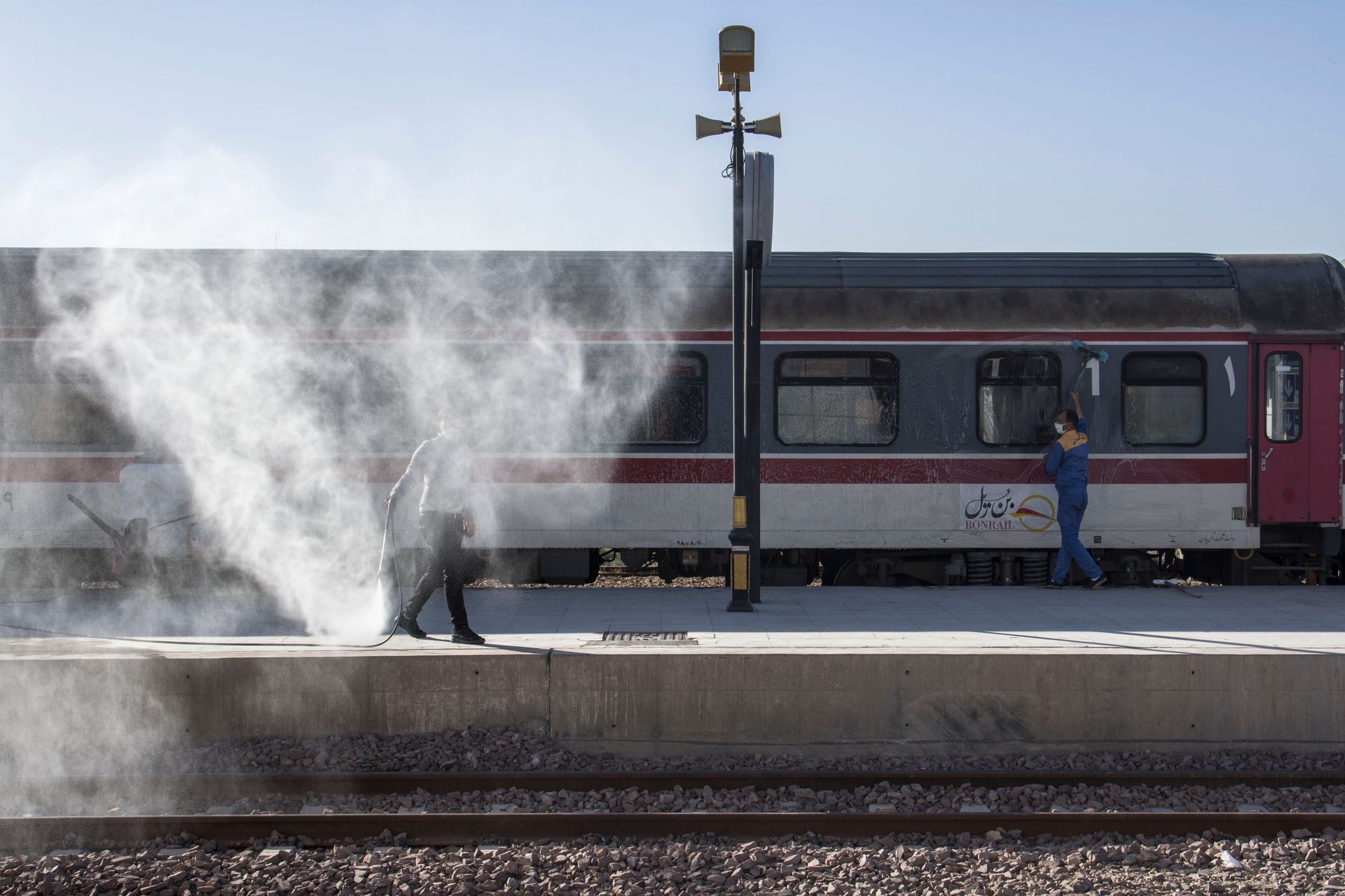 Maintenance workers cleaning a train at a railway station, with one using a water hose.