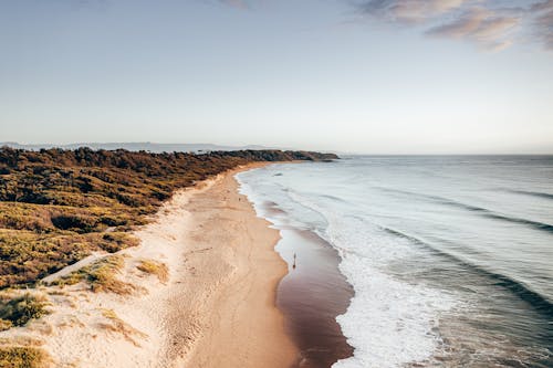 Wavy ocean washing sandy beach on rocky coast under blue sky in sunny day