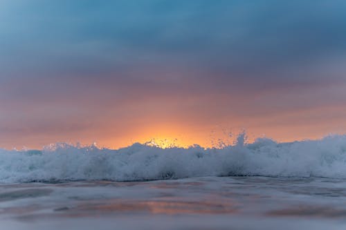 Sunset sky over waving sea washing shore
