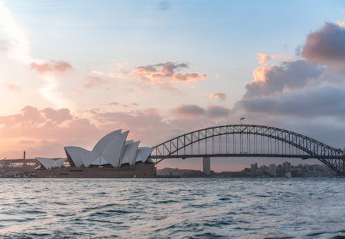Free Amazing cityscape of Sydney with famous Opera House and arched Harbour Bridge connecting districts against picturesque cloudy sunset sky Stock Photo
