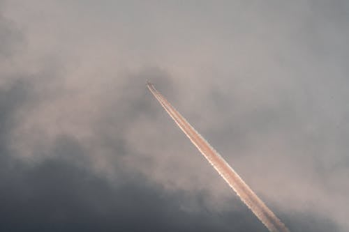 From below of modern aircraft flying in cloudy sunset sky and leaving straight long track
