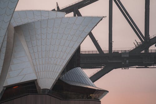 Shells of contemporary white Sydney Opera House facade near large Sydney Harbor Bridge in peaceful twilight