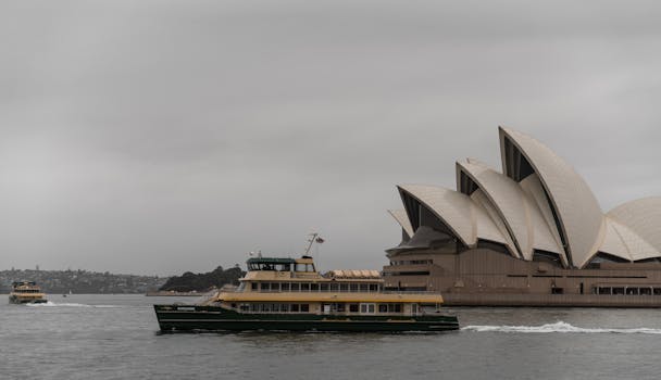 A ferry passes by the iconic Sydney Opera House on a cloudy day.