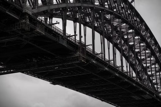 Black and white from below famous Sydney Harbor Bridge with arch trusses beneath gloomy sky