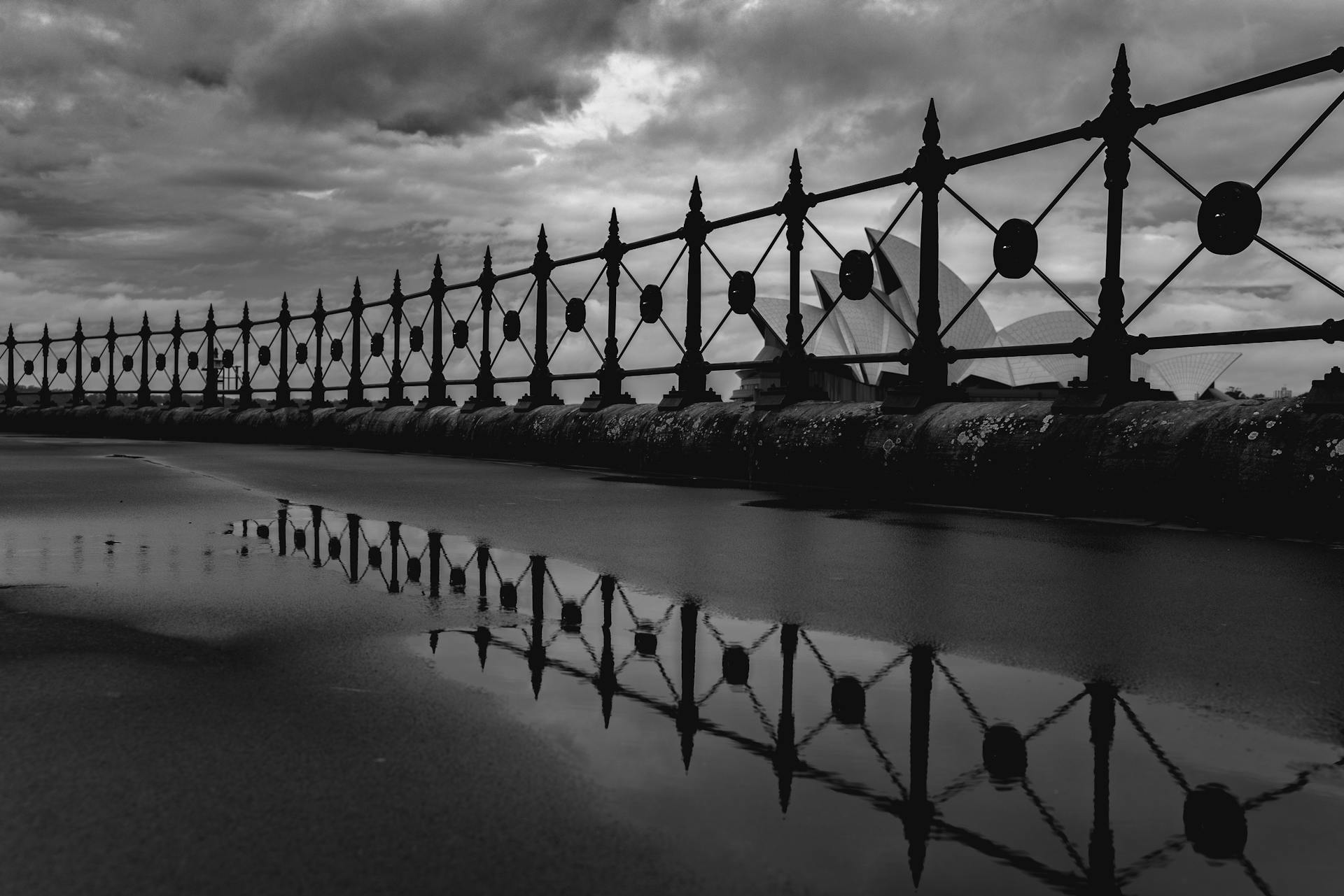 Black and white famous white Sydney Opera House behind embankment metal railing on overcast rainy day