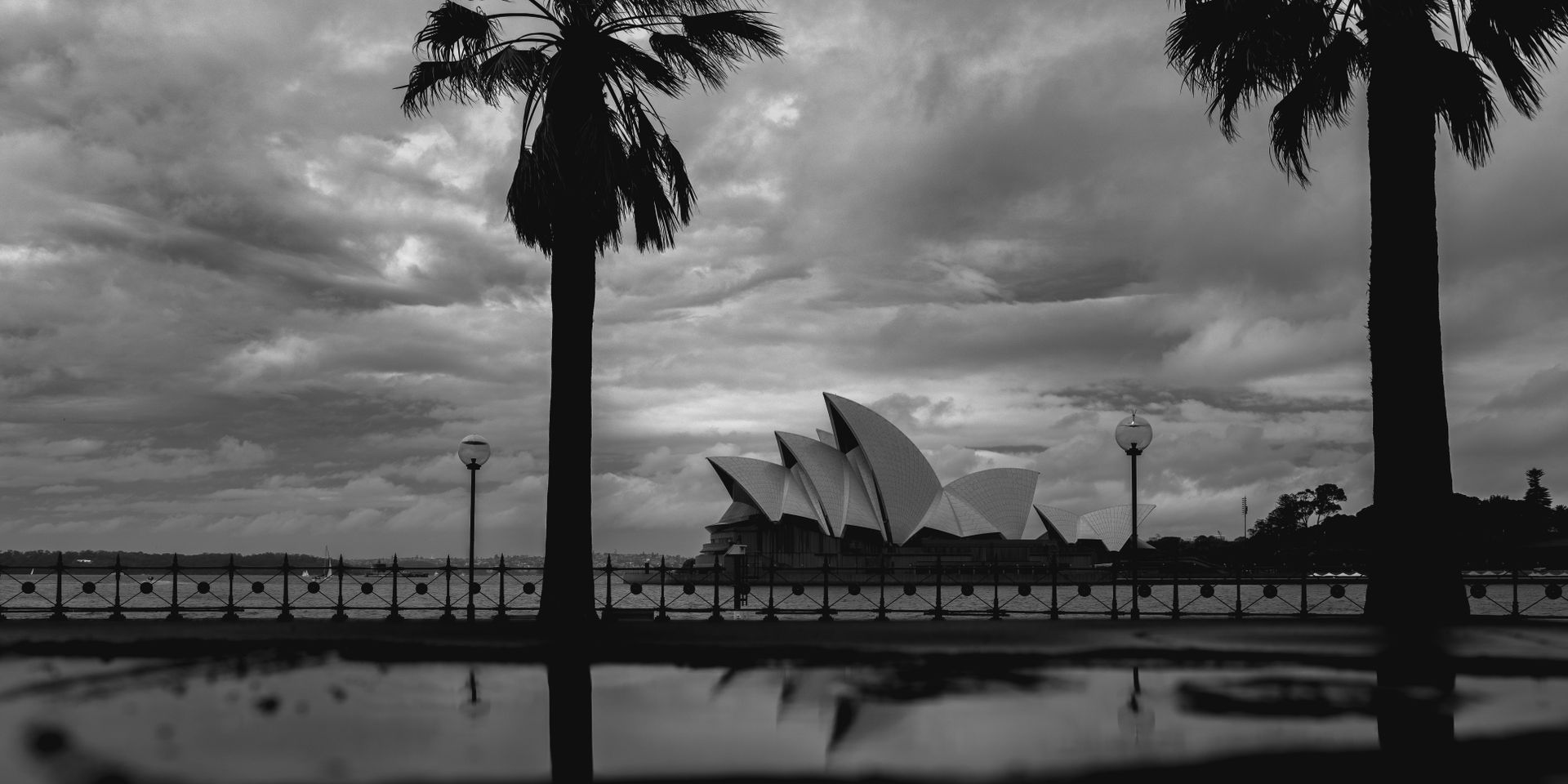 Black and white facade of white geometric Sydney Opera House located near city promenade on cloudy gloomy weather